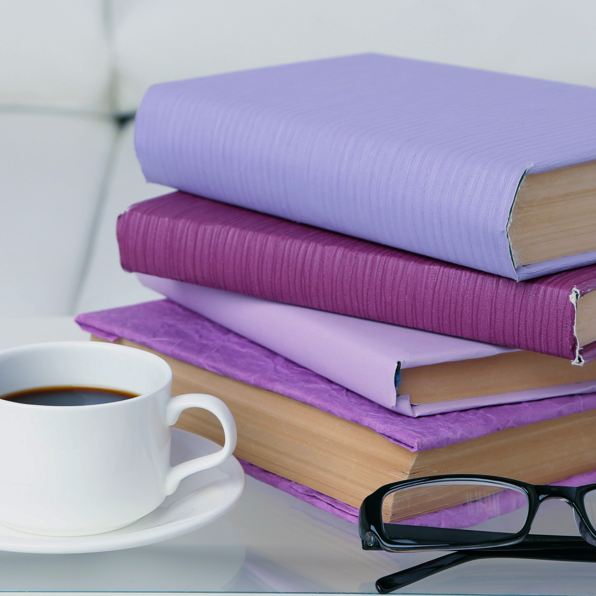 Livres violets empilés avec lunettes et tasse de café